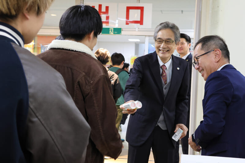 りんごジュースを学生に配布する福田学長と奥田社長
